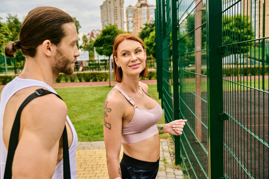 Мужчина и женщина в спортивной одежде стоят рядом с забором, выражая решимость и мотивацию после занятий спортом на открытом воздухе - Фото, изображение
