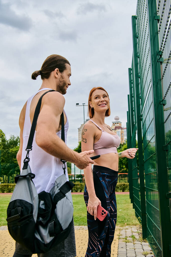 Un homme et une femme déterminés en vêtements de sport se tiennent le long d'une clôture après l'entraînement - Photo, image