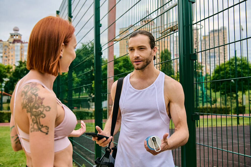 Un hombre y una mujer en ropa deportiva están junto a una valla, motivados por el entrenamiento personal en una sesión de entrenamiento al aire libre. - Foto, imagen
