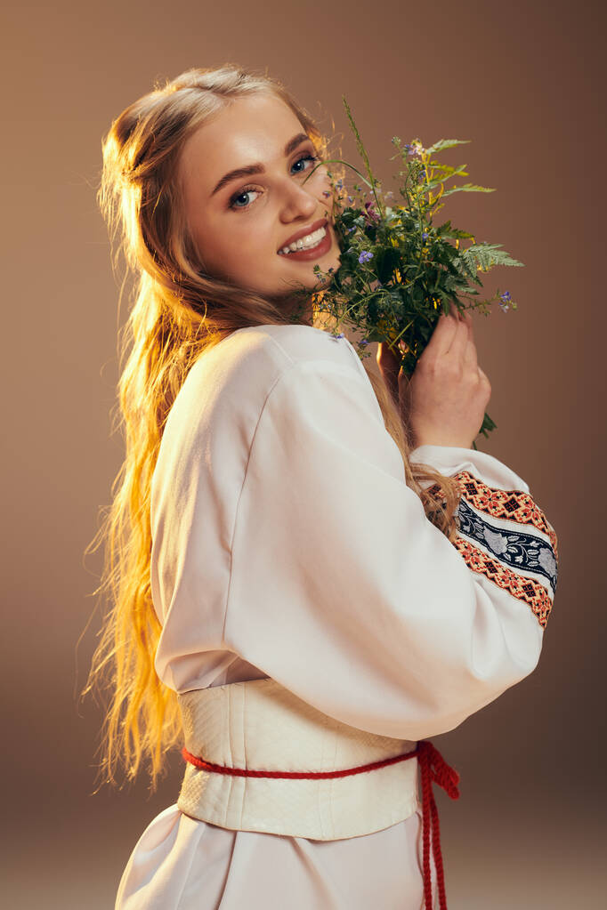 Een jong meisje in een witte jurk houdt subtiel een sierlijke bloem in een serene studio setting. - Foto, afbeelding