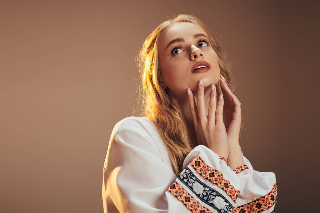 Een jonge vrouw in een wit shirt houdt teder haar handen op haar gezicht, belichaamt kwetsbaarheid en contemplatie in een studio setting. - Foto, afbeelding