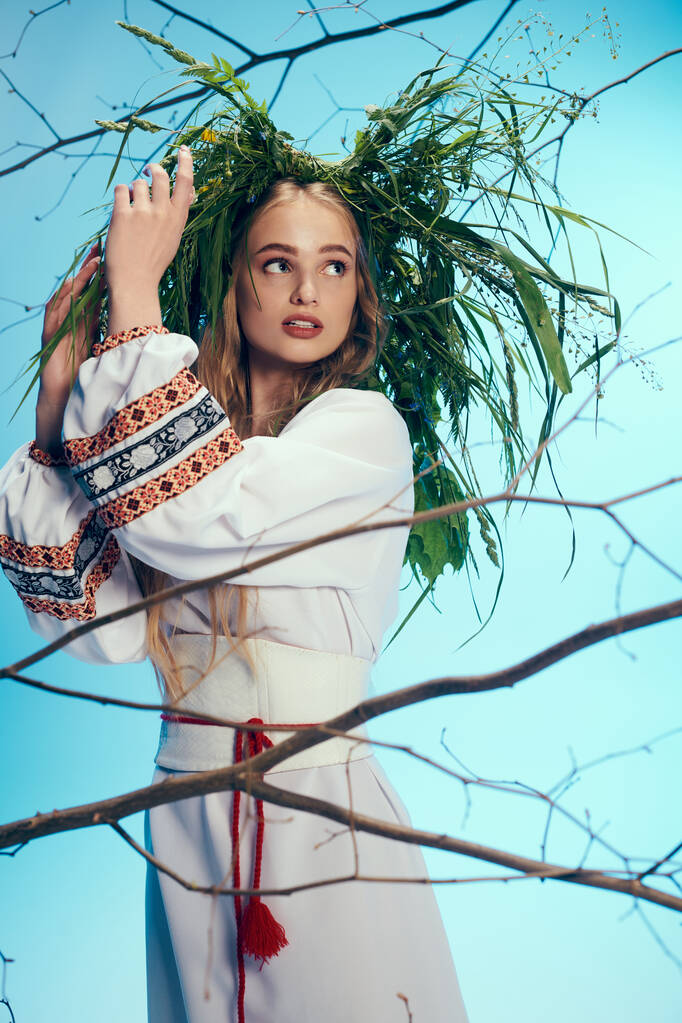 Een jonge mavka in traditionele kledij staat voor een majestueuze boom, met een krans op haar hoofd. - Foto, afbeelding