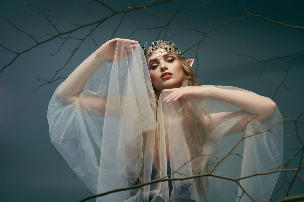 Молода жінка, одягнена як принцеса ельфа, стоїть з вуаллю, що прикрашає голову в містичній студії. - Фото, зображення