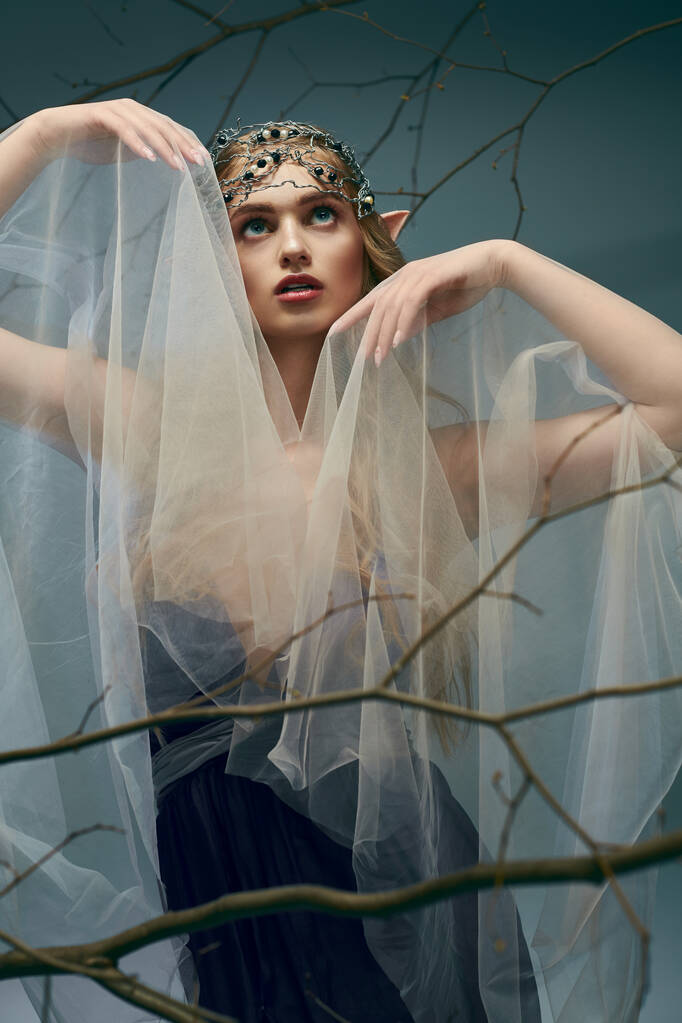 A young woman, dressed as an elf princess, adorns a flowing veil on her head in a studio setting. - Photo, Image