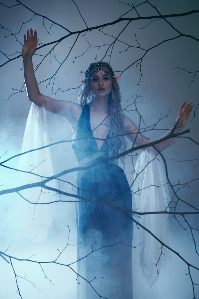 Una giovane donna in un abito blu fluente si erge con grazia di fronte a un albero maestoso, incarnando l'essenza di una principessa fata. - Foto, immagini