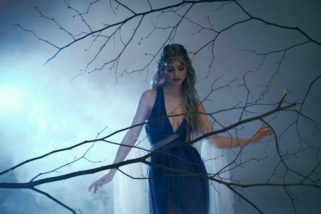 Μια νεαρή γυναίκα με πριγκίπισσα ξωτικό vibes στέκεται με χάρη μπροστά από ένα δέντρο, φορώντας ένα εντυπωσιακό μπλε φόρεμα. - Φωτογραφία, εικόνα