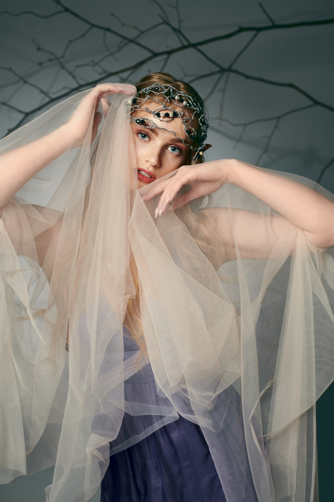 Молодая женщина в платье с вуалью, украшающей ее голову, выглядит как принцесса-фея в воображаемой обстановке. - Фото, изображение