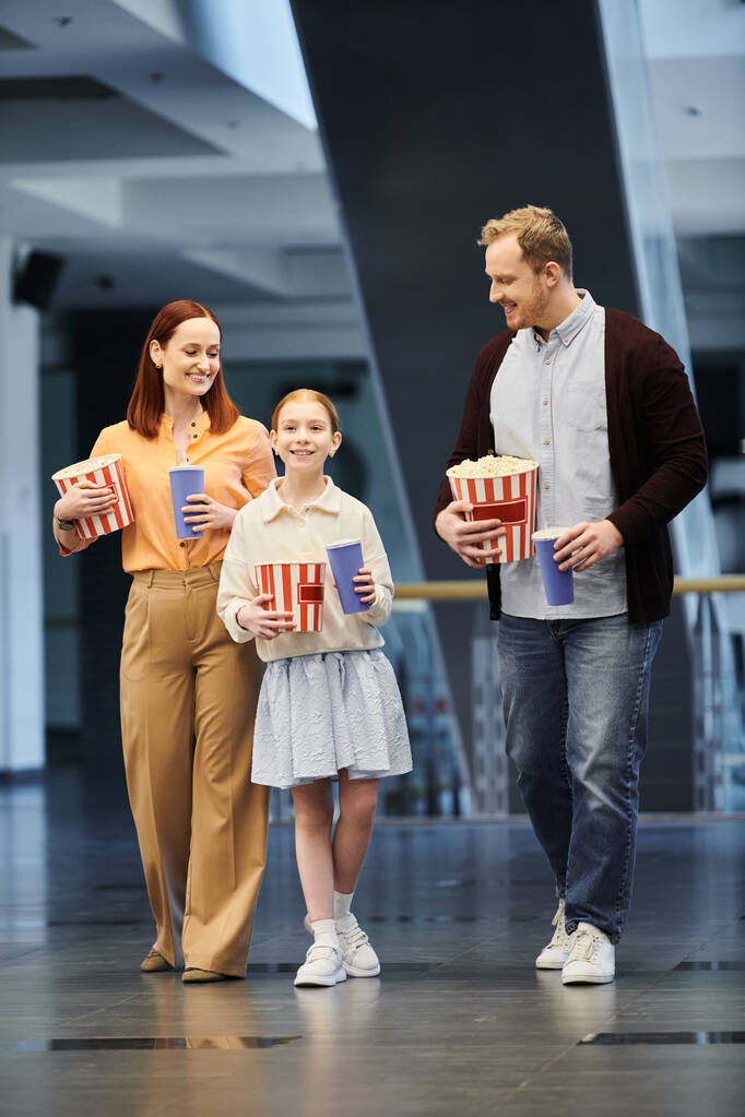 Muž, žena a dítě radostně drží popcorn boxy, když spolu tráví čas v kině. - Fotografie, Obrázek