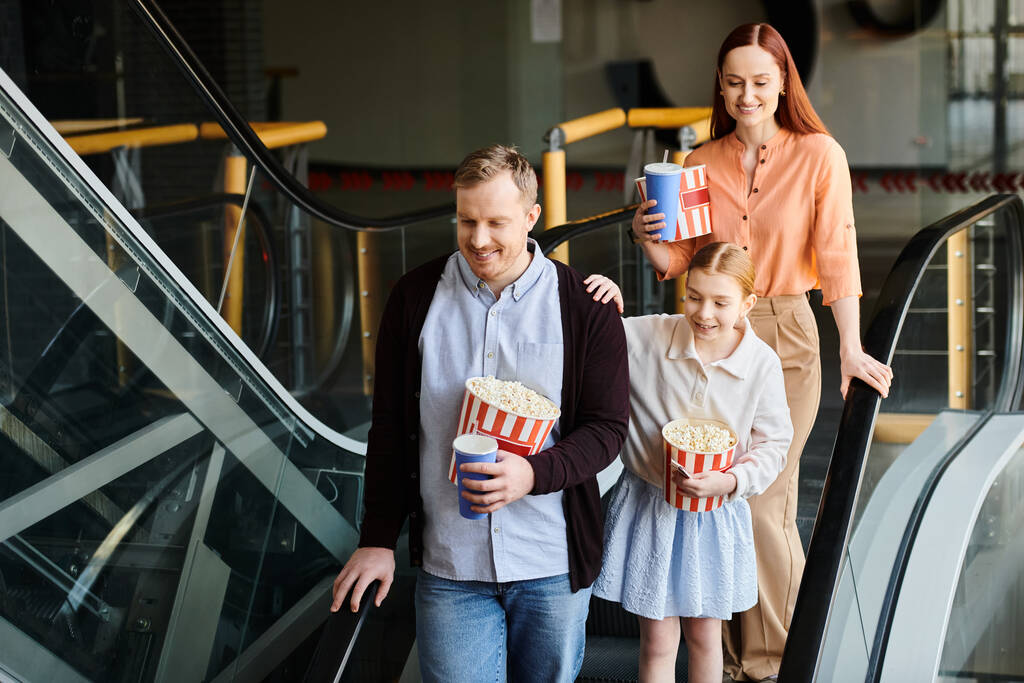 Un homme et deux petites filles descendent joyeusement un escalier roulant ensemble dans un cinéma, créant une scène de famille chaleureuse. - Photo, image