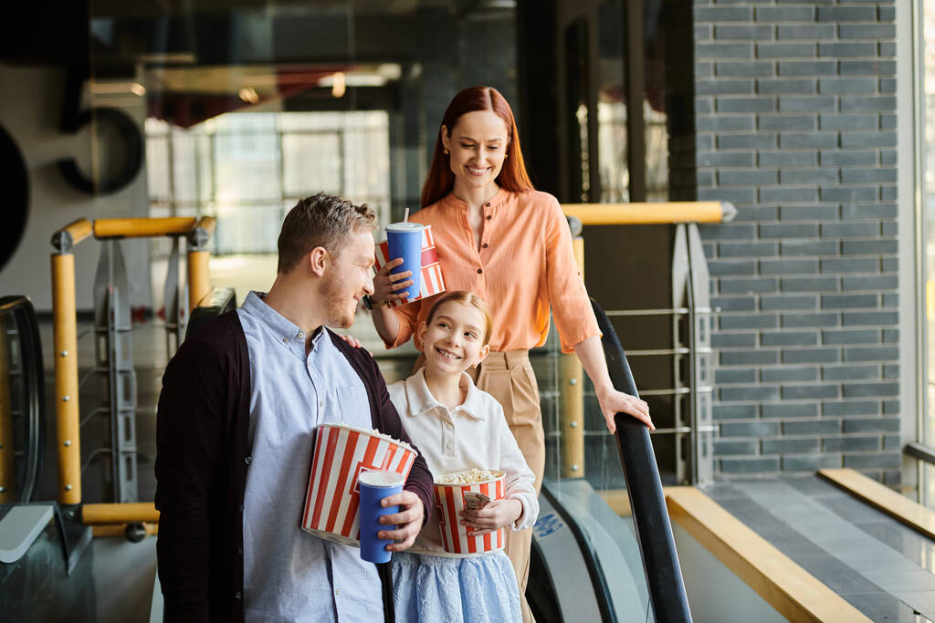 Ένας άντρας, μια γυναίκα και ένα παιδί στέκονται έξω από ένα σινεμά, ενθουσιασμένοι να περάσουν ποιοτικό οικογενειακό χρόνο μαζί βλέποντας μια ταινία.. - Φωτογραφία, εικόνα