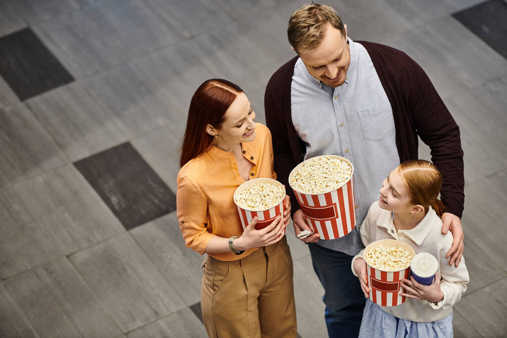 Un uomo e sua moglie tengono gioiosamente scatole di popcorn con bambino mentre si godono un film insieme al cinema. - Foto, immagini