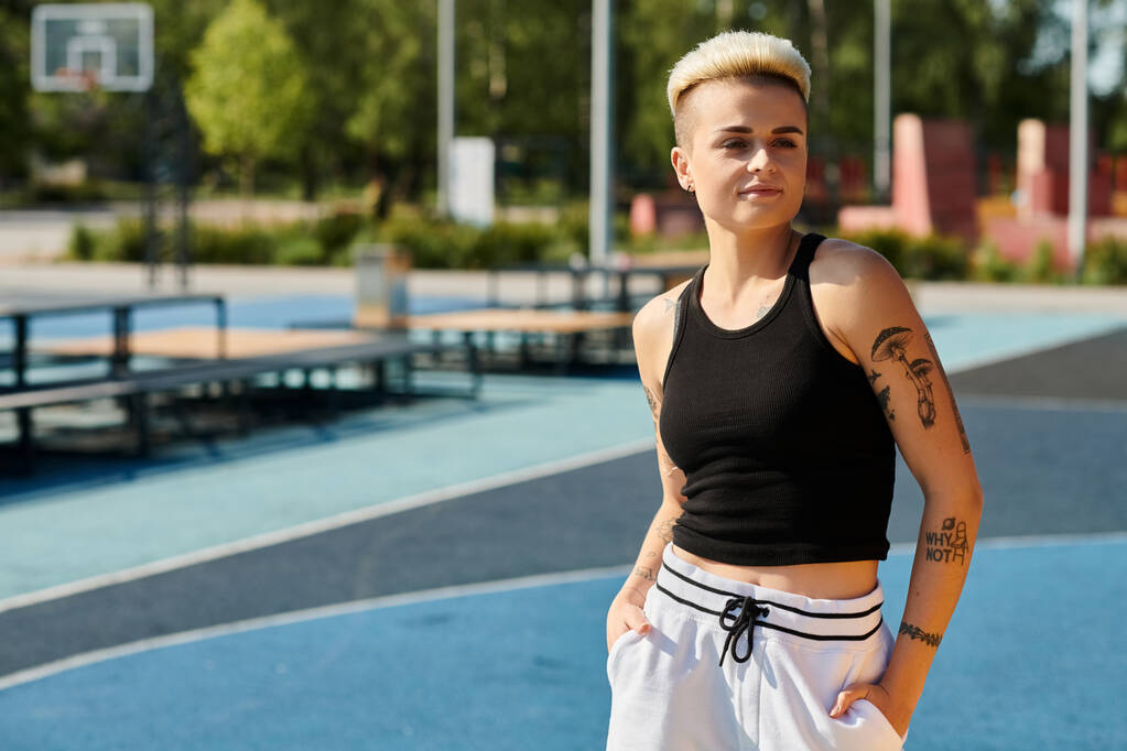 Молода жінка з коротким волоссям і татуюваннями стоїть на баскетбольному майданчику, руки в кишенях, виключаючи впевненість і спокій. - Фото, зображення