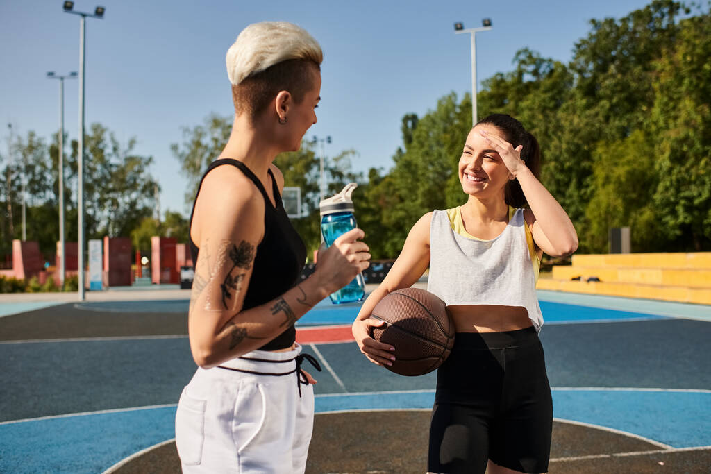 Ένας άνδρας και μια γυναίκα στέκονται με αυτοπεποίθηση σε ένα γήπεδο μπάσκετ, επιδεικνύοντας τον αθλητισμό και την ομαδικότητα τους σε ένα ζωηρό παιχνίδι.. - Φωτογραφία, εικόνα