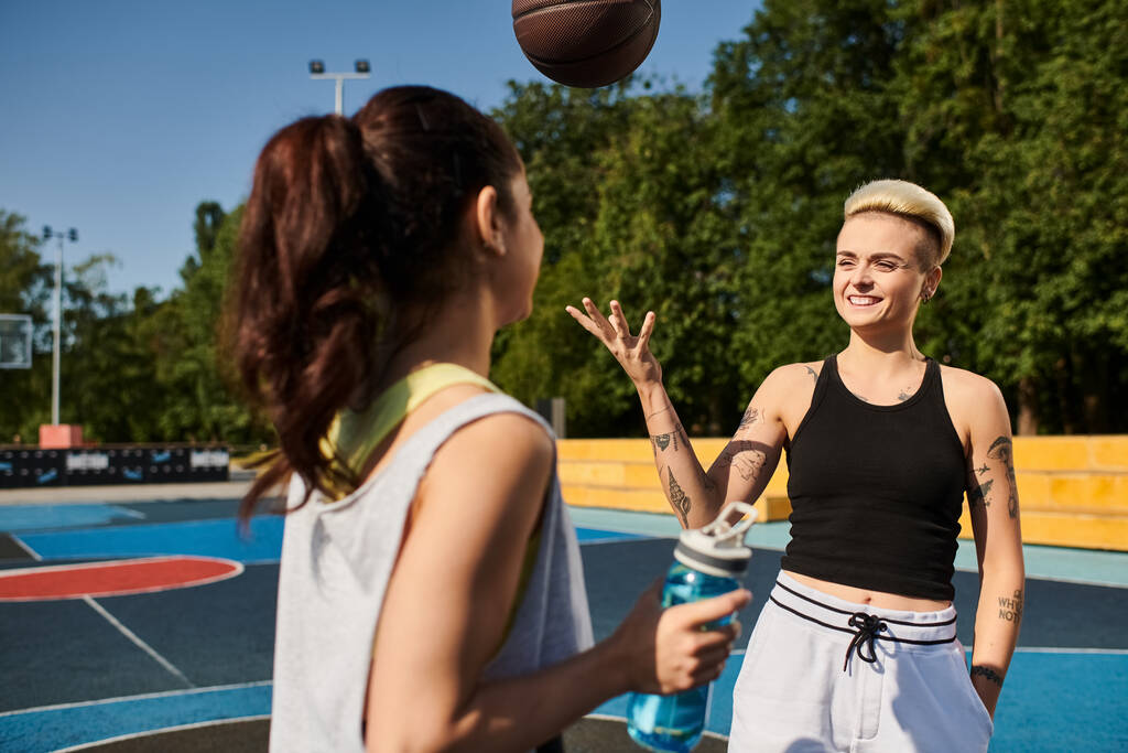 Una joven mujer se para con confianza frente a un baloncesto en una soleada cancha al aire libre. - Foto, Imagen