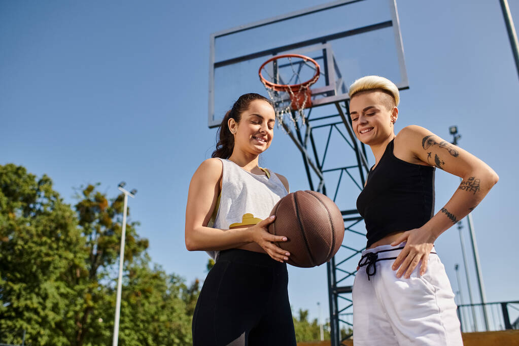 Dos mujeres jóvenes atléticas goteando un baloncesto al aire libre en un día soleado, disfrutando de un juego amistoso juntas. - Foto, Imagen