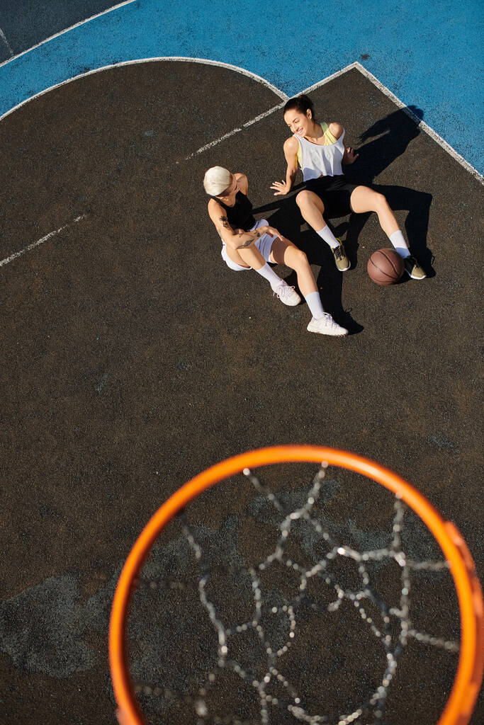 Dvě mladé ženy vítězoslavně stojí na basketbalovém hřišti a oslavují své vítězství s úsměvem za slunečného letního dne. - Fotografie, Obrázek