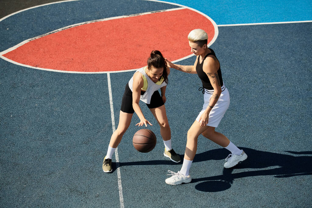 Twee atletische jonge vrouwen staan trots op een basketbalveld en stralen zelfvertrouwen en sportiviteit uit op een zonnige dag.. - Foto, afbeelding