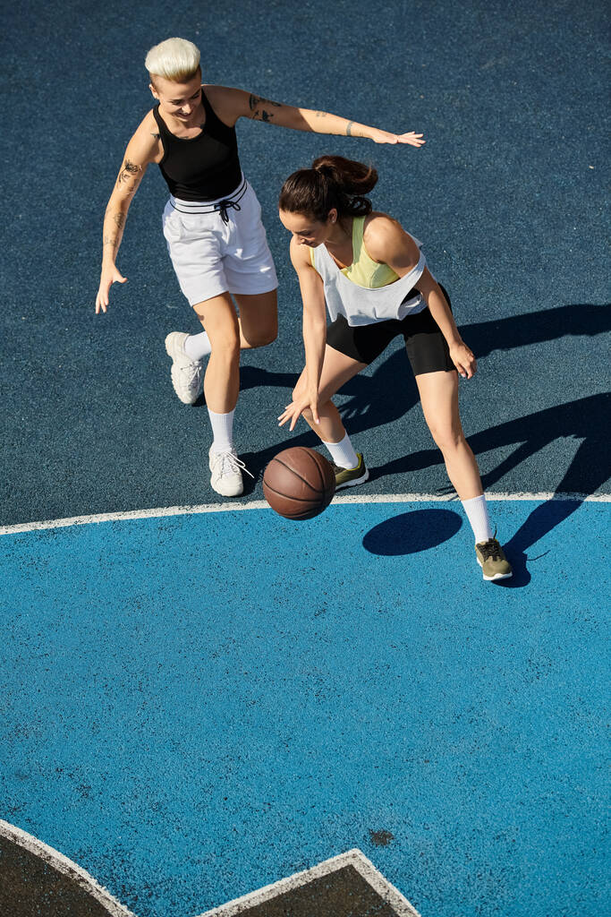Deux amies sportives sont immergées dans un jeu compétitif de basket-ball sur un terrain extérieur pendant l'été. - Photo, image