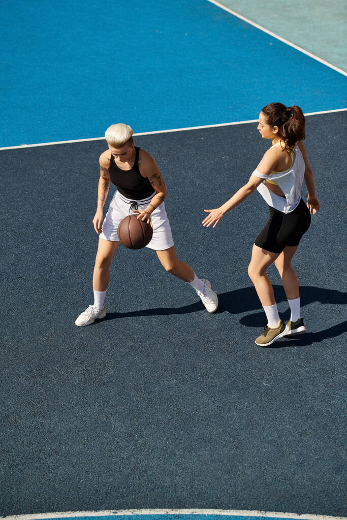 Mujeres jóvenes atléticas jugando al baloncesto al aire libre en un día soleado, mostrando sus habilidades y trabajo en equipo. - Foto, imagen