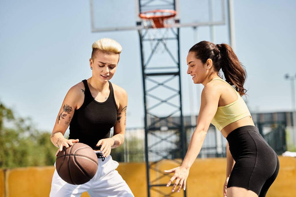 Deux jeunes femmes se tiennent côte à côte à l'extérieur, tenant un ballon de basket alors qu'elles aiment un jeu de cerceaux au soleil d'été. - Photo, image
