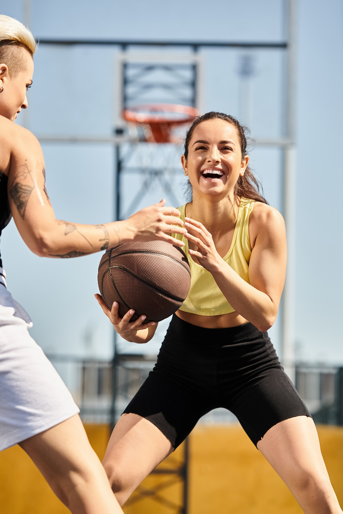 Deux jeunes femmes sportives debout ensemble, dont une tenant un ballon de basket-ball, prêtes à jouer au basket-ball dehors par une journée ensoleillée en été. - Photo, image