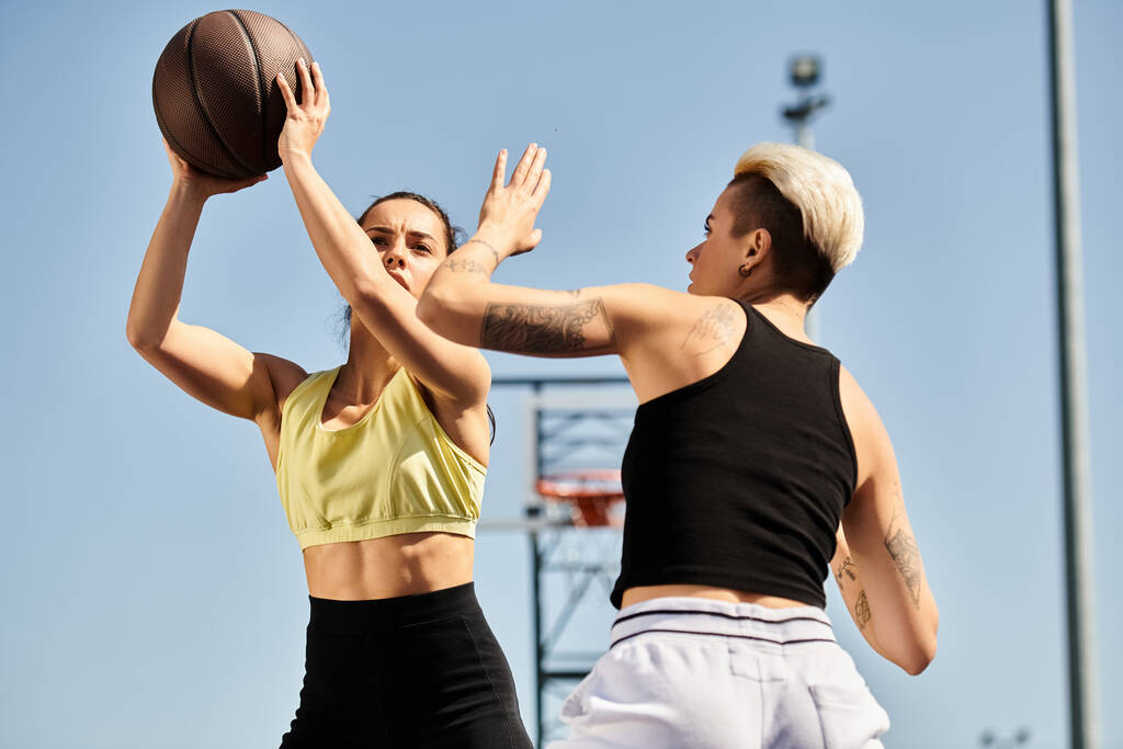 Dwie młode kobiety stojące obok siebie, energicznie trzymające koszykówkę, cieszące się sportową chwilą na świeżym powietrzu latem. - Zdjęcie, obraz