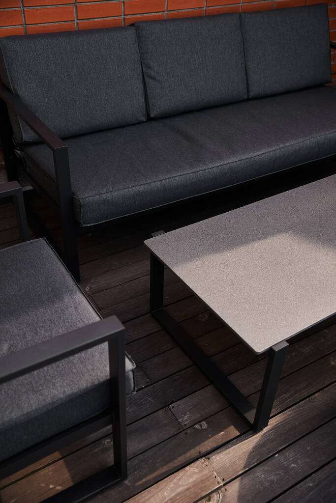 Un canapé élégant et un mobilier de table moderne sur une terrasse en bois altérée dans un espace extérieur tranquille - Photo, image