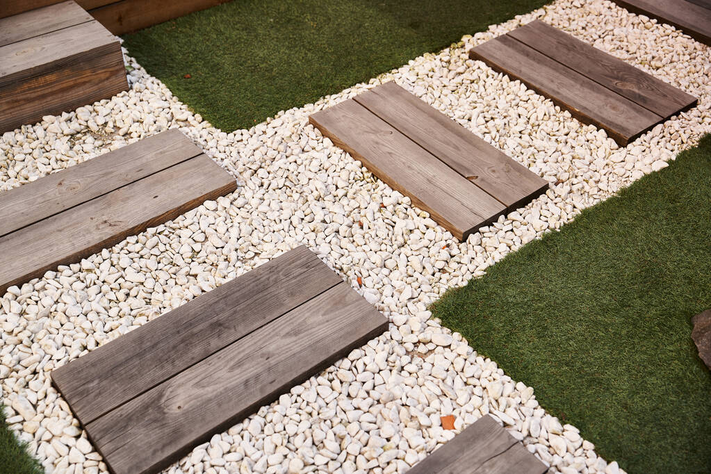 Um sereno espaço de jardim com degraus de madeira que levam até um caminho de cascalho cercado por verdura exuberante e elementos decorativos - Foto, Imagem