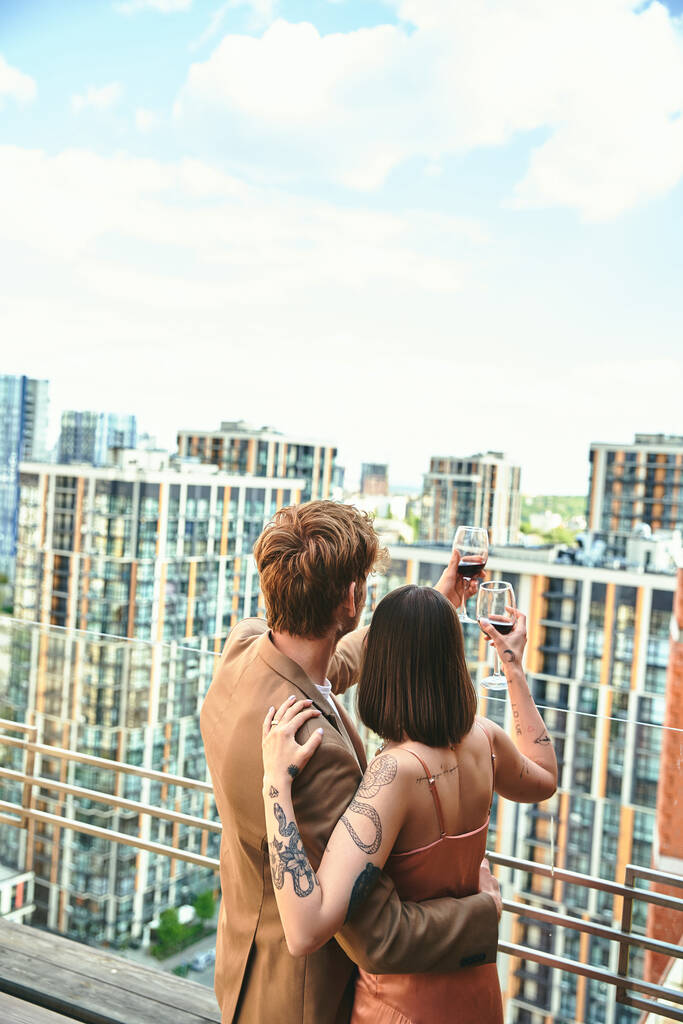 Молодая пара, поднятые бокалы, тосты за жизнь на фоне оживленного городского пейзажа. - Фото, изображение