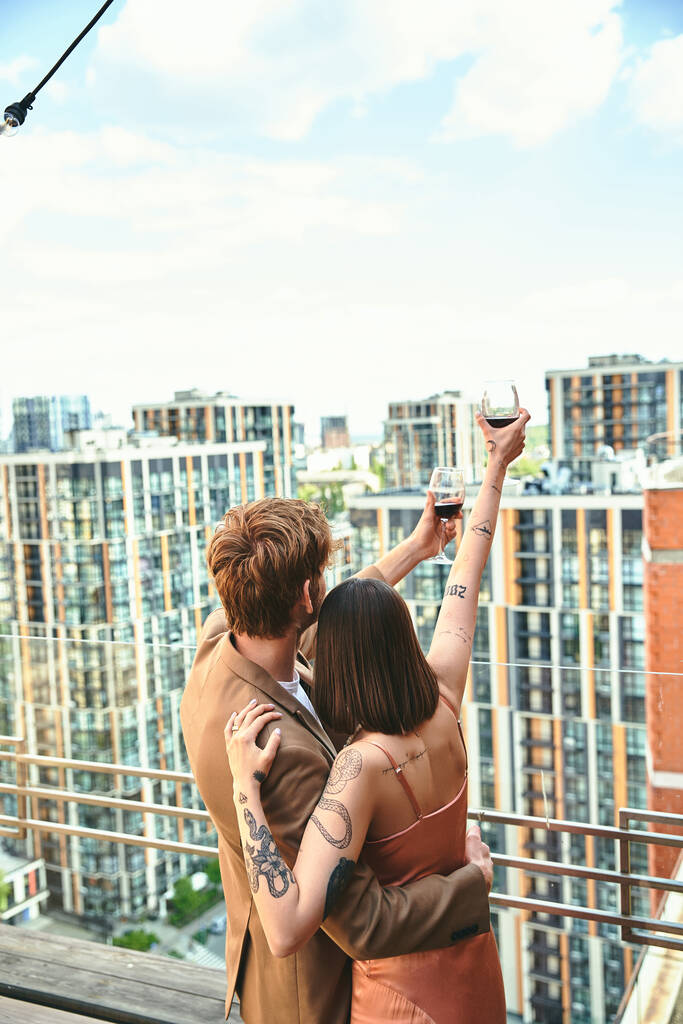 Muž a žena stojí sebevědomě na okraji tyčící se budovy a objímají městskou krajinu rozprostírající se před nimi - Fotografie, Obrázek