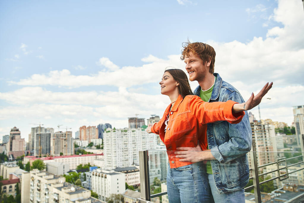 Egy férfi és egy nő magabiztosan áll egy tornyosuló épület tetején, és bámulja a várost odalent, a szabadság és a kapcsolat érzésével. - Fotó, kép