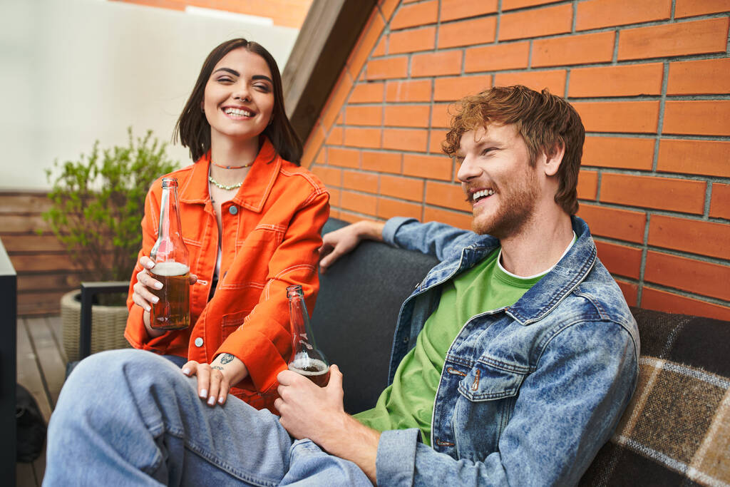 Dos amigos, disfrutando de risas y conversaciones, disfrutan de bebidas refrescantes en un acogedor sofá al aire libre - Foto, imagen