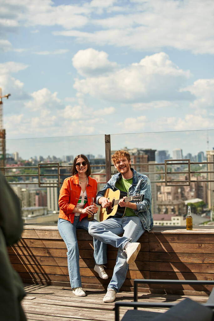 Mężczyzna i kobieta siedzą na ławce, grając zsynchronizowane gitary, tworząc harmonijną melodię w spokojnym otoczeniu - Zdjęcie, obraz