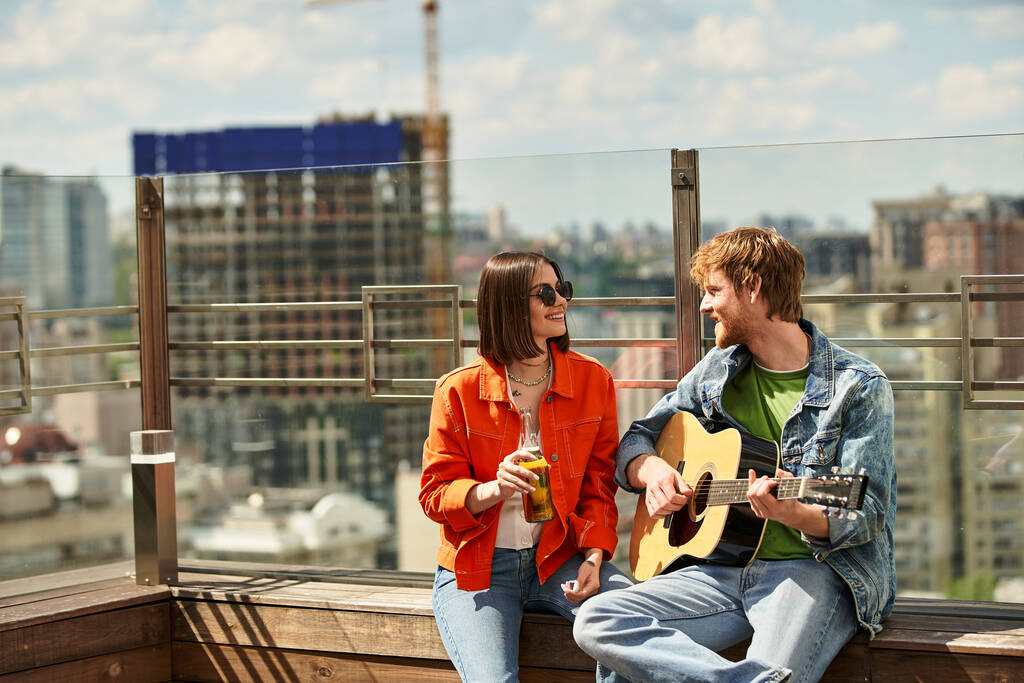 男性と女性がリッジに座り,ギターを弾くことに魅了され,穏やかな背景の中で美しい調和を作り出します. - 写真・画像