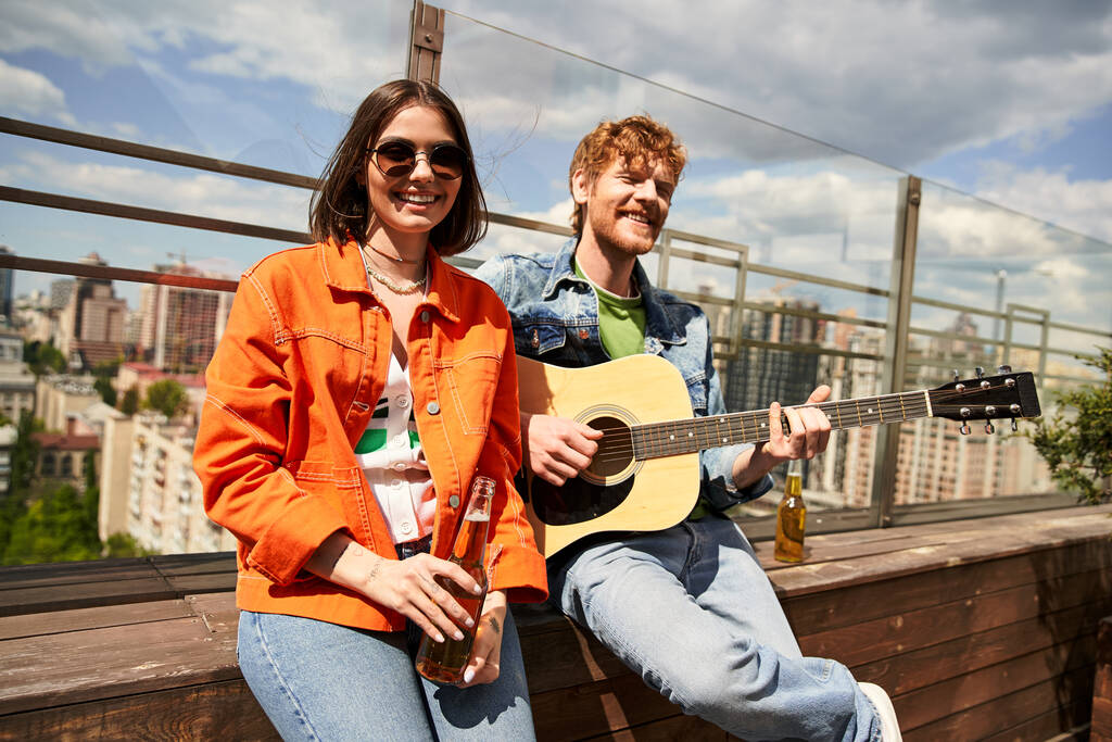 Мужчина и женщина сидят на выступе, вместе играют на гитаре под звездным небом, создавая романтическую и мелодичную атмосферу. - Фото, изображение
