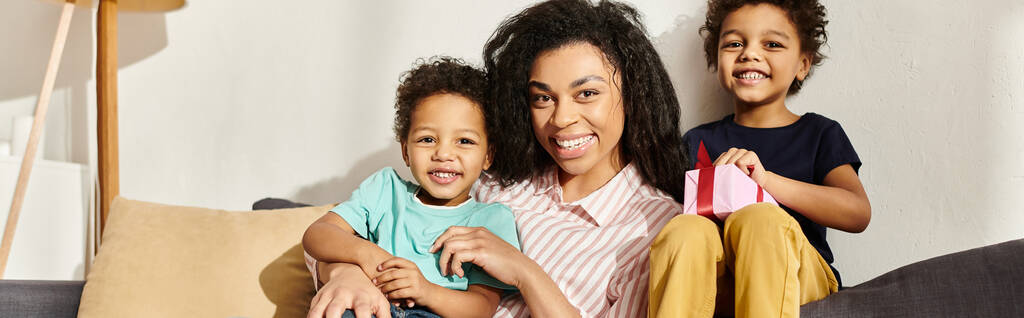 alegre familia afroamericana de tres sonriendo a cámara, presente en la mano, día de la madre, estandarte - Foto, Imagen