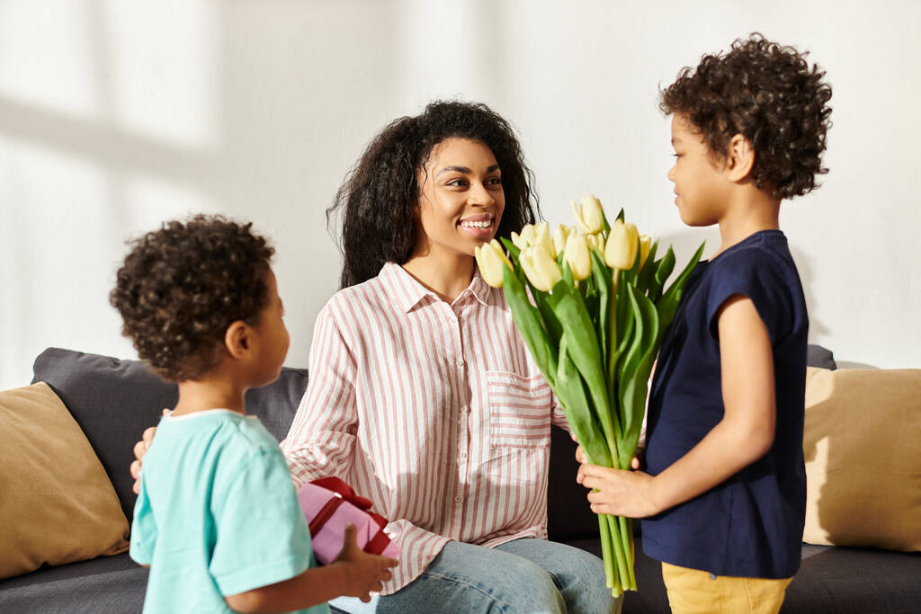 gyönyörű vidám afro-amerikai nő kap ajándékot és tulipán az ő kis fiai, Anyák napja - Fotó, kép