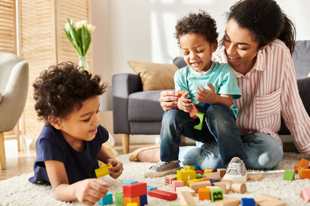 приваблива афроамериканська жінка, яка активно грає зі своїми маленькими синами, перебуваючи вдома - Фото, зображення