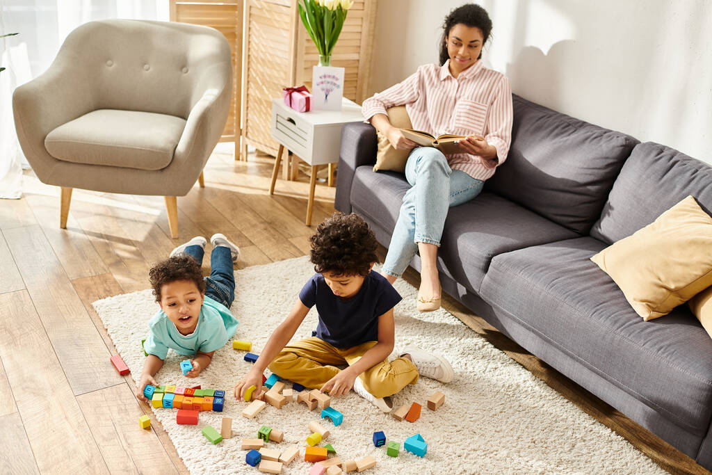 alegre africana americana madre mirando a sus hijos jugando con juguetes mientras ella leyendo libro - Foto, Imagen