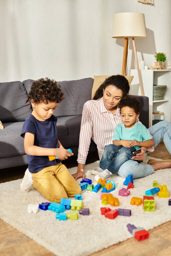 alegre bela mãe afro-americana assistindo seus adoráveis filhinhos brincando com brinquedos em casa - Foto, Imagem