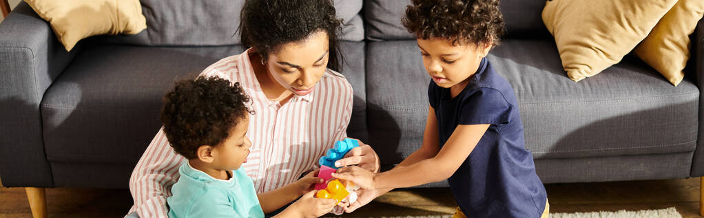bien parecido afroamericano madre jugando con sus lindos hijos pequeños en sala de estar, pancarta - Foto, Imagen