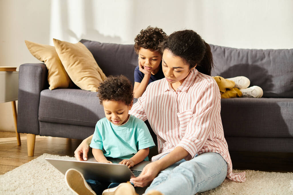 schöne afrikanisch-amerikanische Frau in Homewear, die Filme auf dem Laptop mit ihren beiden lustigen Söhnen anschaut - Foto, Bild