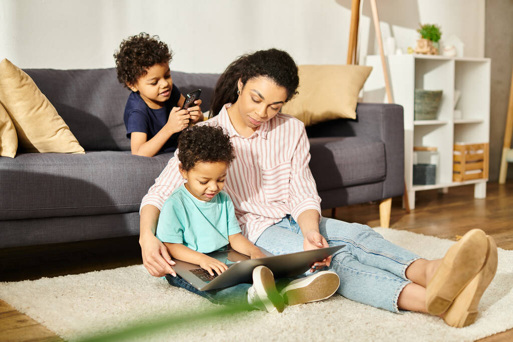 attraente afro americano madre in accogliente homewear guardare film con i suoi figli svegli sul computer portatile - Foto, immagini