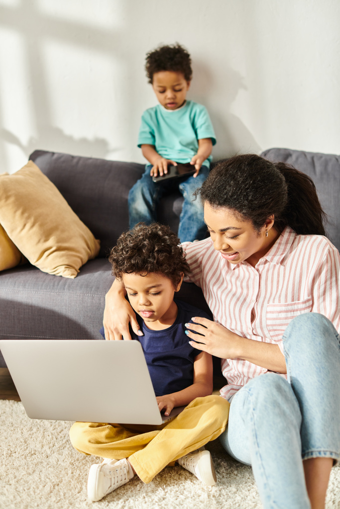 Neşeli Afro-Amerikalı kadın dizüstü bilgisayarı ve telefonu olan iki sevimli oğluyla vakit geçiriyor. - Fotoğraf, Görsel