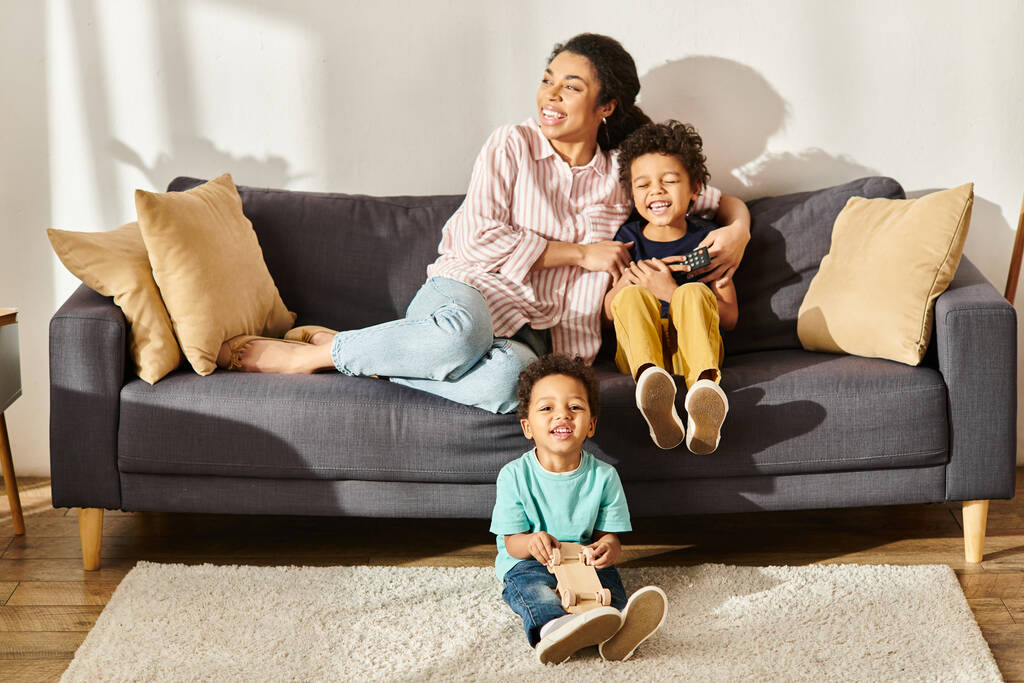 alegre afroamericano chico jugando juguete de madera coche al lado de su madre y hermano sentado en sofá - Foto, imagen