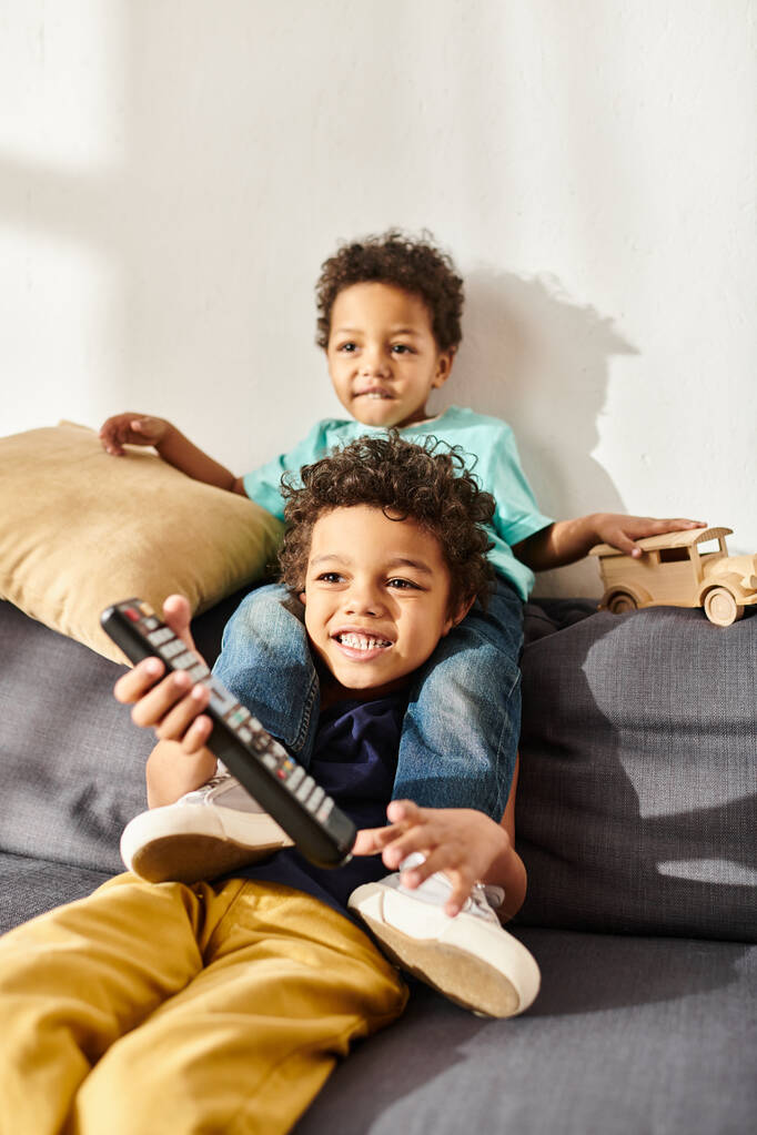 merry african american cute boys holding remote control and wooden toy car and watching movies - Photo, Image