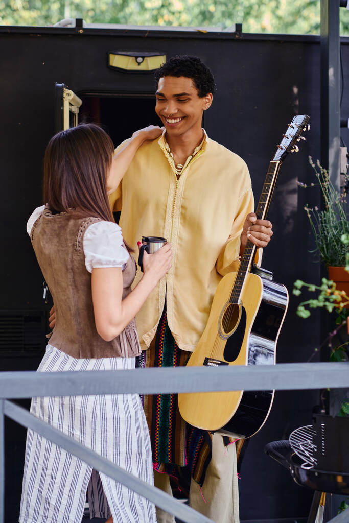 Un uomo serenata una donna con una chitarra in un ambiente naturale vicino a un camper, creando un'atmosfera romantica. - Foto, immagini