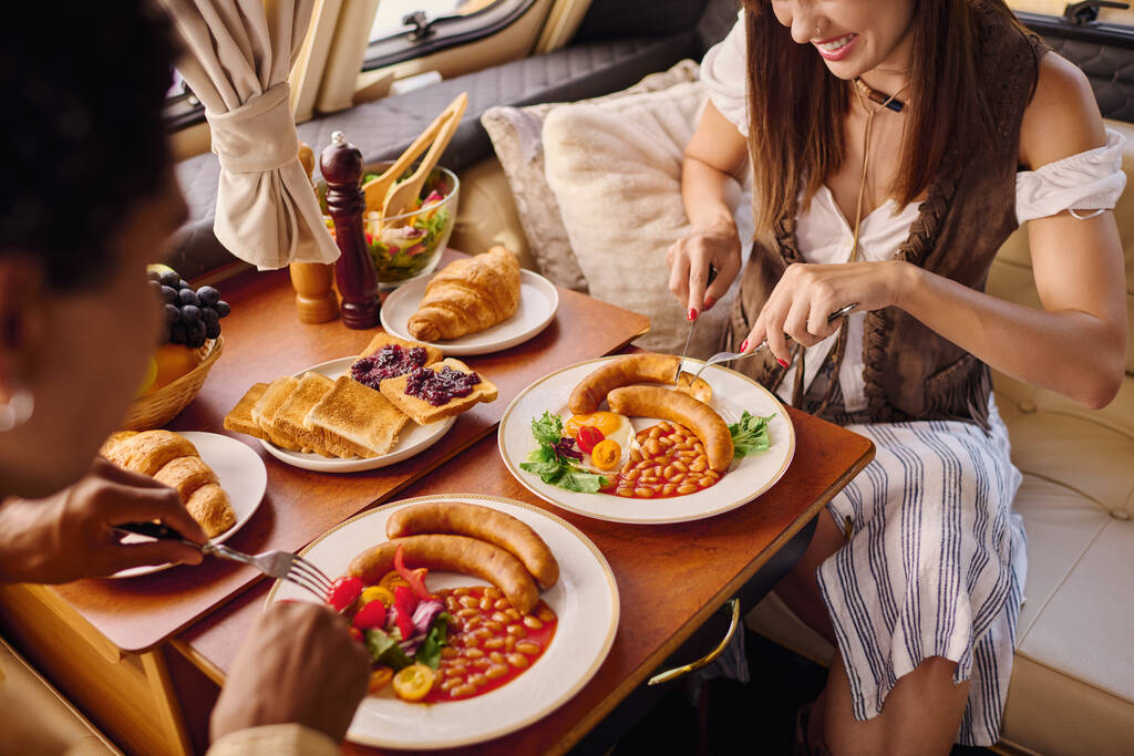 Egy nő ül az asztalnál, élvezi a különböző finom ételeket szétszórva előtte egy romantikus menekülés során egy lakókocsiban. - Fotó, kép