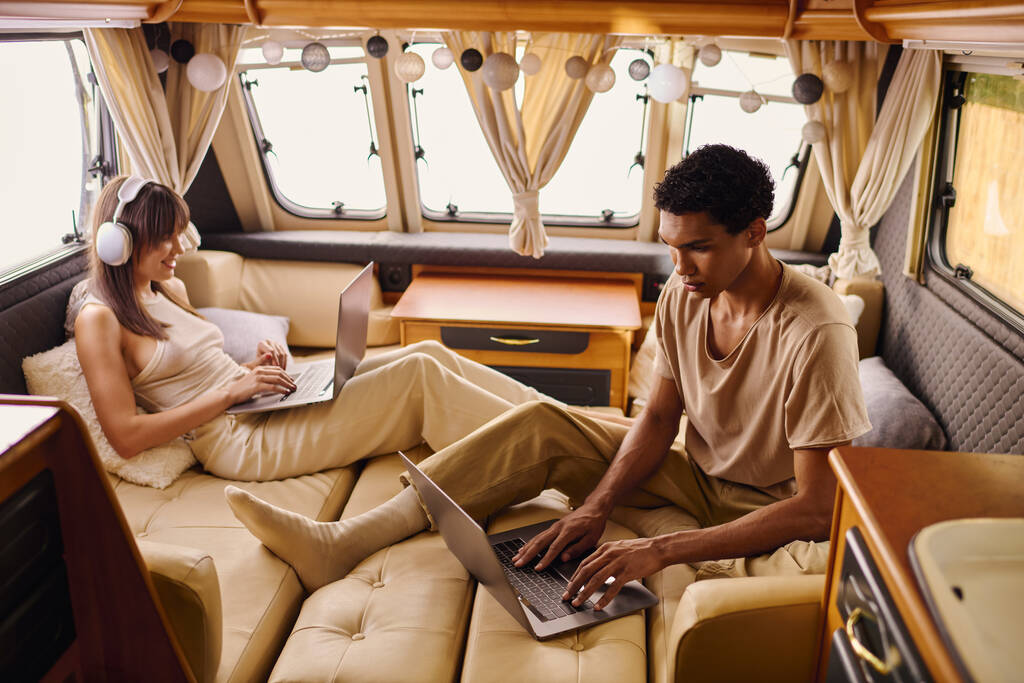 Un hombre y una mujer se sientan en un sofá, cada uno absorto en sus computadoras portátiles, con expresiones enfocadas. - Foto, imagen
