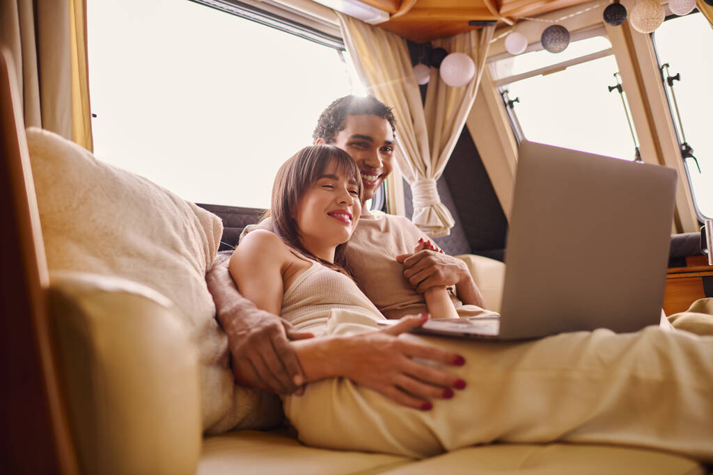 Un uomo e una donna si siedono strettamente su un divano, entrambi concentrati su uno schermo del computer portatile di fronte a loro. - Foto, immagini